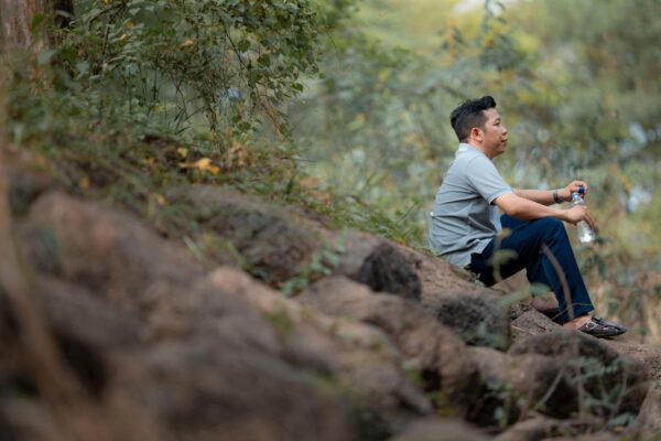 A man sits on rocks with a water bottle, surrounded by greenery in a forest in Bien Hoa, Vietnam.